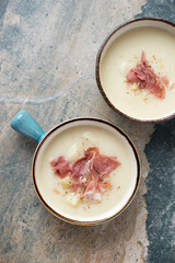 Potato soup topped with torn prosciutto, vertical shot on a beige and grey granite background with space, above view