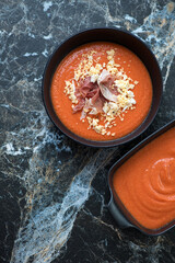 Bowl of salmorejo or cold spanish tomato and bread soup, top view on a black marble background, vertical shot with space