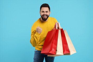 Excited man with many paper shopping bags on light blue background