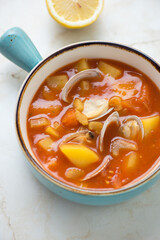 Manhattan chowder with vongole clams in a turquoise serving bowl, vertical shot on a light-beige marble surface, middle close-up