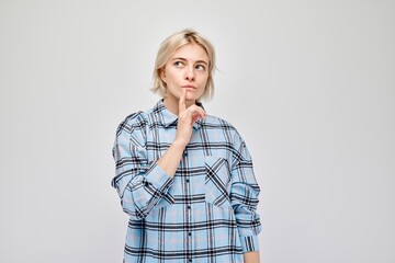 Thoughtful woman in plaid shirt with finger on lips, contemplating, on a light background.