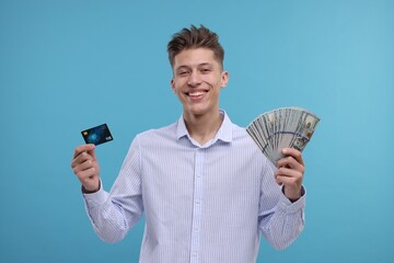 Happy man with credit card and dollar banknotes on light blue background