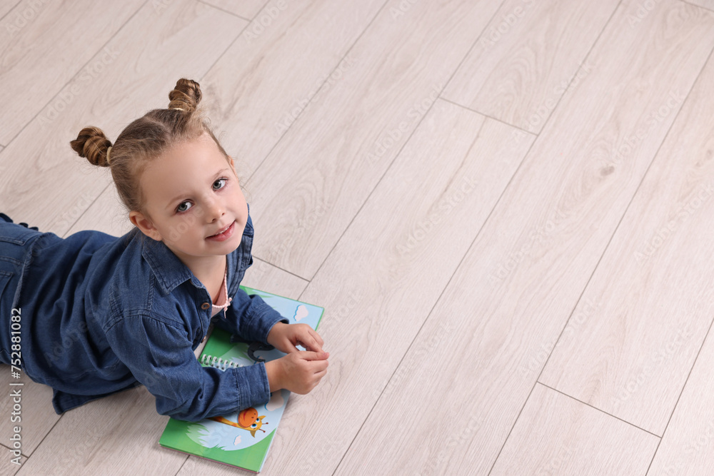 Wall mural Cute little girl with book on warm floor at home, space for text. Heating system