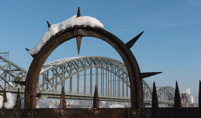 Detail eines Zauns mit Schnee und der Kölner Südbrücke im Hintergrund