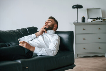 On the black sofa. Upset young man drinker alcoholic is indoors