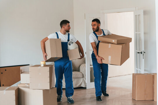 Front view, holding stuff. Two moving service employees in a room