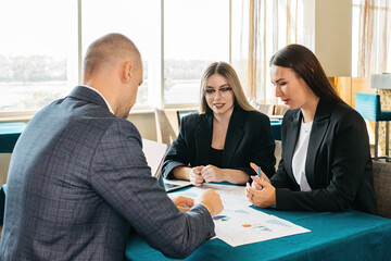 A group of people in a modern coworking space discuss the tasks and business processes of the team. Collection of managers or analytics. Growth analysis, chart, statistics and data. People work in a b