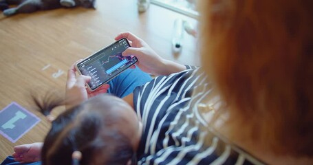 A woman trades stocks on a mobile device while caring for an infant at home - Powered by Adobe