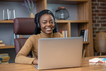 Professional businesswoman with dreadlocks in headphones uses laptop for online teaching