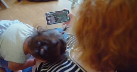A woman trades stocks on a mobile device while caring for an infant at home - Powered by Adobe