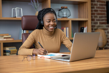 Adult woman with dreadlocks in headphones works as a virtual tech trainer using laptop