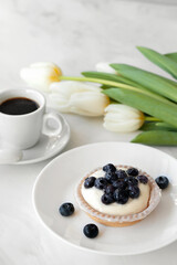 Panna cotta with blueberries on plate, cup of coffee and flowers on white table, traditional Italian sweet milky dessert