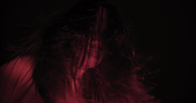 A woman ghost with hair over their face with wind blowing illuminated by a red light creating a haunting effect. Halloween holiday