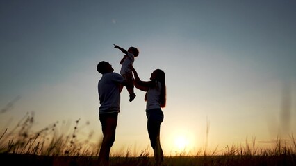 family standing on the field. happy childhood concept for little child. big happy family stands on field, parents raised the lifestyle child in their arms, sunset on the background, silhouettes © maxximmm