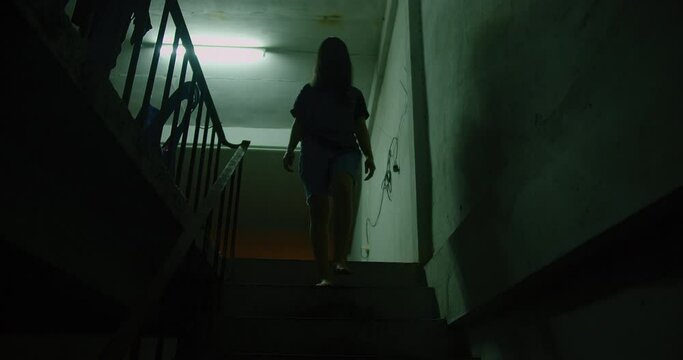A woman ghost is walking down a dark stairwell. The image has a moody scary horror creepy darkness and eerie atmosphere, Halloween holidays concept