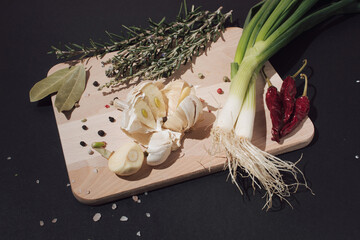 Wooden kitchen board with garlic, onion, chili peppers, bay leaf and rosemary. Healthy food concept.