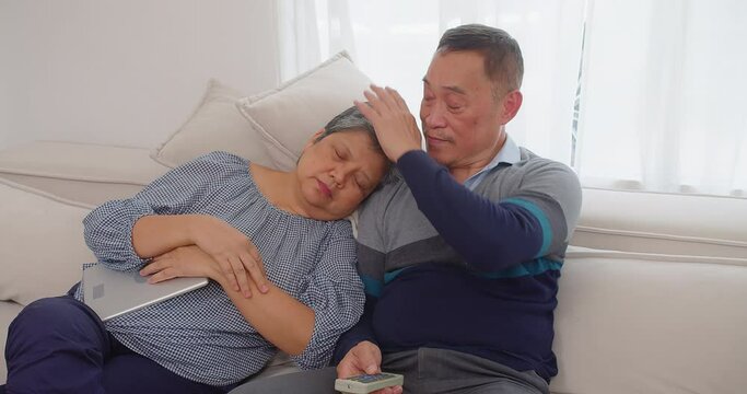 Senior Retirement Asian Married Couple Resting On A Couch, The Man Comforting The Woman Who Has A Headache.