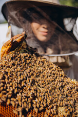 Close-up female Beekeeper in protective suit holding honeybee frame with bees at apiary