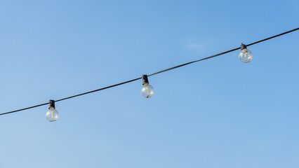 landscape location photography The blue sky was clear during the day, with faint clouds interspersed by black wires or strings holding three small, round, clear bulbs. that have not yet been activated