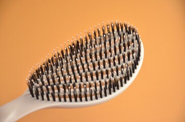 New beige oval hairbrush with bristles on an orange background, closeup