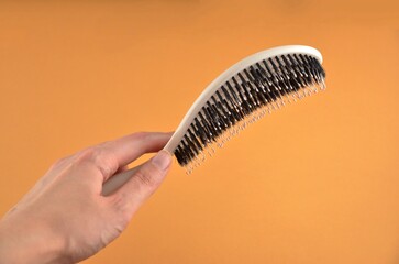 New beige oval hairbrush with bristles in a hand on an orange background