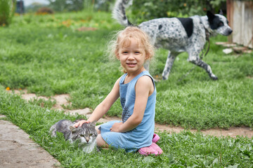Curly-haired girl stroking a cat in the grass on a summer day.
