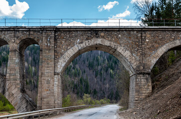 A stone bridge over a forest mountain road in the form of an arched viaduct