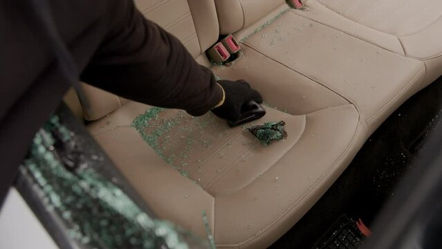 A wallet left on the beige leather back seat is stolen through a broken window, capturing the aftermath of a reckless theft. The scene depicts the brazen act with vivid clarity