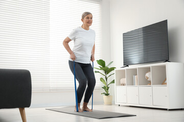 Senior woman doing exercise with fitness elastic band on mat at home