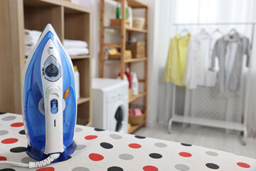 Clothes iron on ironing board in laundry room, space for text