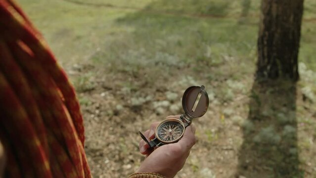 Over the shoulder close up shot of hands of male hiker using compass for navigation while traveling in nature on summer day