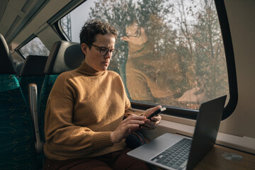 Woman working on smartphone and laptop while traveling by train