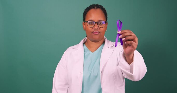 Black female doctor holding purple awareness ribbon, serious in white coat