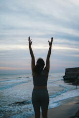 Fototapeta na wymiar Chica realizando poses de yoga y mudras en la playa al atardecer en tonos marrones