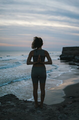 Chica realizando poses de yoga y mudras en la playa al atardecer en tonos marrones