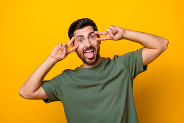 Fototapeta na wymiar Photo of excited carefree man wear khaki t-shirt showing two v-signs cover eyes isolated yellow color background