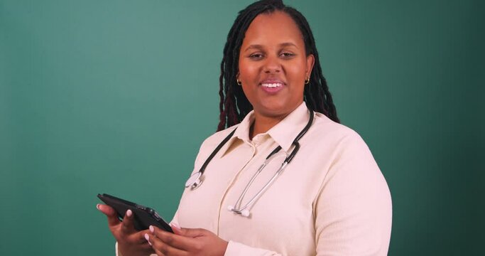 Young Black female doctor works on tablet, smiles at the camera