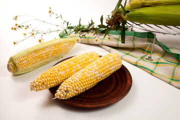 Clay plate with two cobs sweet corn on white wooden background..