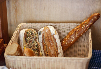 Freshly baked breads placed inside a woven basket. The breads have different shapes and toppings, bakery items, whole grain, adorned with various seeds and herbs on its crust. Rustic brown bread - Powered by Adobe
