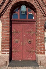 Red door with arch window on top and decorative large metal hinges and knocker.