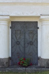 Fototapeta premium A decorative metal double doors with flowers in a vase at a old stone building.