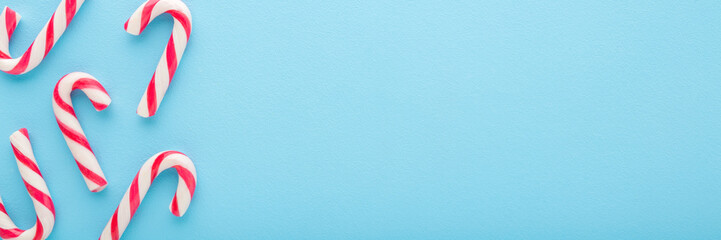 Red white candy canes on light blue table background. Pastel color. Closeup. Sweets wide banner. Empty place for text. Top down view.