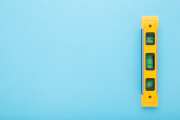 New yellow spirit level on light blue table background. Pastel color. Closeup. Building tool for...