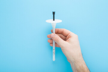 Young adult man hand fingers holding and showing new white plastic insulation anchor dowel for styrofoam panels on light blue table background. Pastel color. Closeup. Top down view.