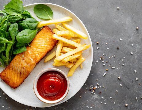 Delicious fish and chips with ketchup, spinach and lettuce on gray table, top view. Space for text