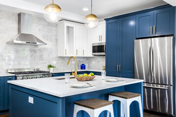 A luxurious white and blue kitchen with gold hardware, stainless steel appliances, and white...