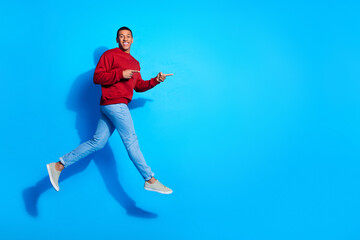 Full length profile photo of handsome guy jump indicate fingers empty space isolated on blue color...