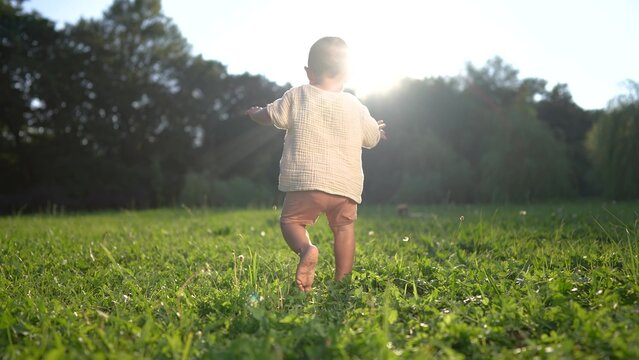 baby takes first steps in the park. happy family kid dream concept. dad teaches his son to walk takes the first steps in the park on lifestyle green grass. baby son taking first steps