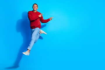 Full size photo of carefree handsome guy jump indicate fingers empty space isolated on blue color...