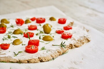 Preparing a focaccia with cherry tomatoes and olives and rosemary leaves.